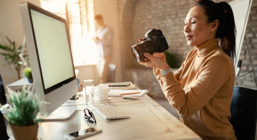produtora de conteúdo digital segurando uma câmera profissional em frente de um monitor