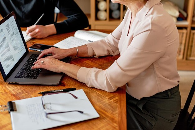 two women sit at a desk with a laptop and a notepad with the word quot on it